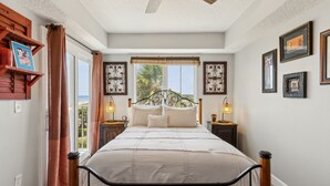 A bedroom with a bed, a ceiling fan, a window with curtains, and framed pictures on the wall. - Vintage Ocean View Paradise - 1BR - Beachfront (Fernandina Beach)