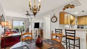 A dining area with a round table, chairs, and a chandelier. There is a kitchen with wooden cabinets and a clock on the wall. - Vintage Ocean View Paradise - 1BR - Beachfront (Fernandina Beach)