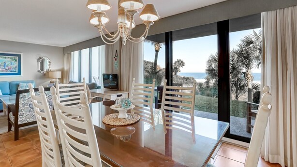 A dining area with a glass table, white chairs, and a chandelier. - Pet Friendly 2 Bedroom Villa w/ Pool - Captain's Court (Fernandina Beach)