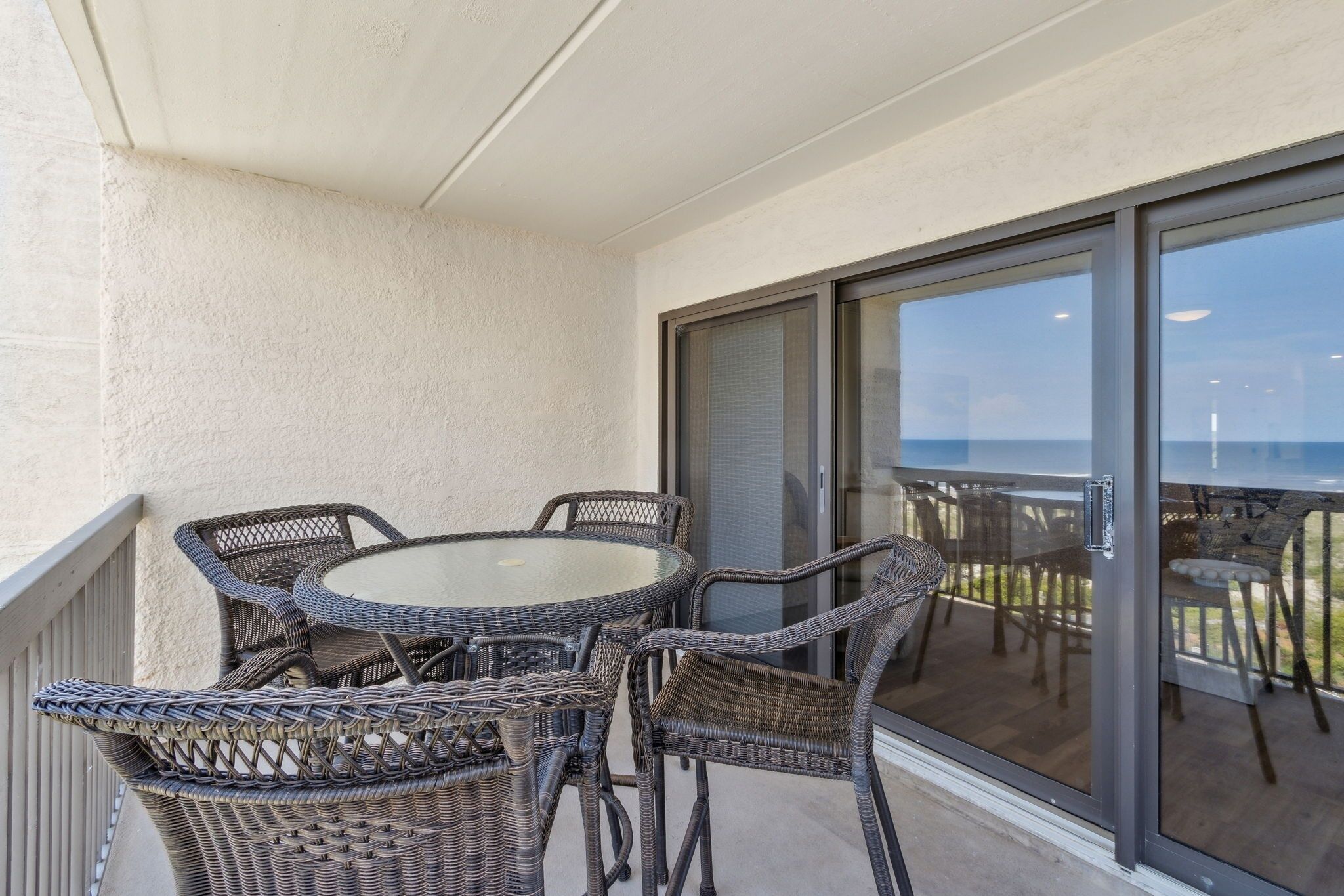 A covered outdoor area with wicker furniture, a glass door leading to a balcony, and a view of the ocean.