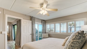 A bedroom with a bed, a ceiling fan, a window with blinds, and a view of the outdoors. - Ground Floor Beachfront Condo Amelia by the Sea (Fernandina Beach)
