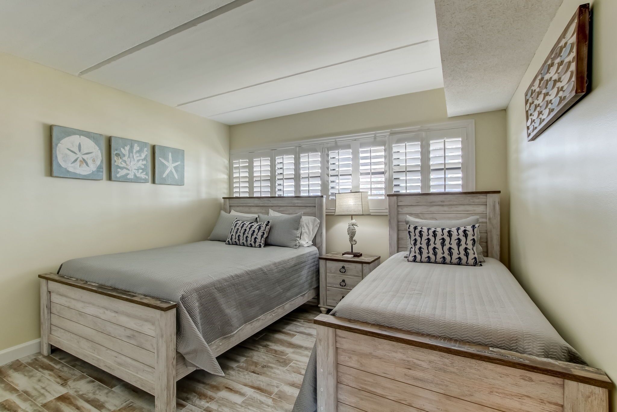 A bedroom with two beds, a nightstand, a window with blinds, and wall art.