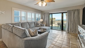 A living room with a grey sectional sofa, a small round table, and a ceiling fan. There is a sliding glass door leading to a balcony with a view of the ocean. - Ground Floor Beachfront Condo Amelia by the Sea (Fernandina Beach)