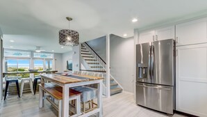 A modern kitchen with a stainless steel refrigerator, a dining area with a wooden table and chairs, and a staircase leading to another level. - Spacious Beachfront 3BR in Amelia Island Sandpiper Loop (Fernandina Beach)