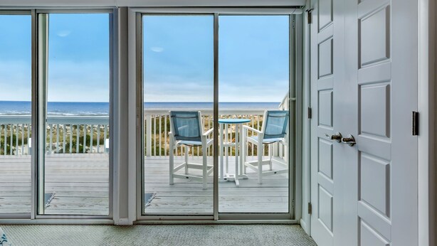 A room with a sliding glass door leading to a deck with a view of the ocean and beach. - Spacious Beachfront 3BR in Amelia Island Sandpiper Loop (Fernandina Beach)