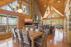 A spacious wooden cabin with a dining area, fireplace, and large windows. - Pine Cone Cabin 4 Bedroom Cabin (Sevierville)