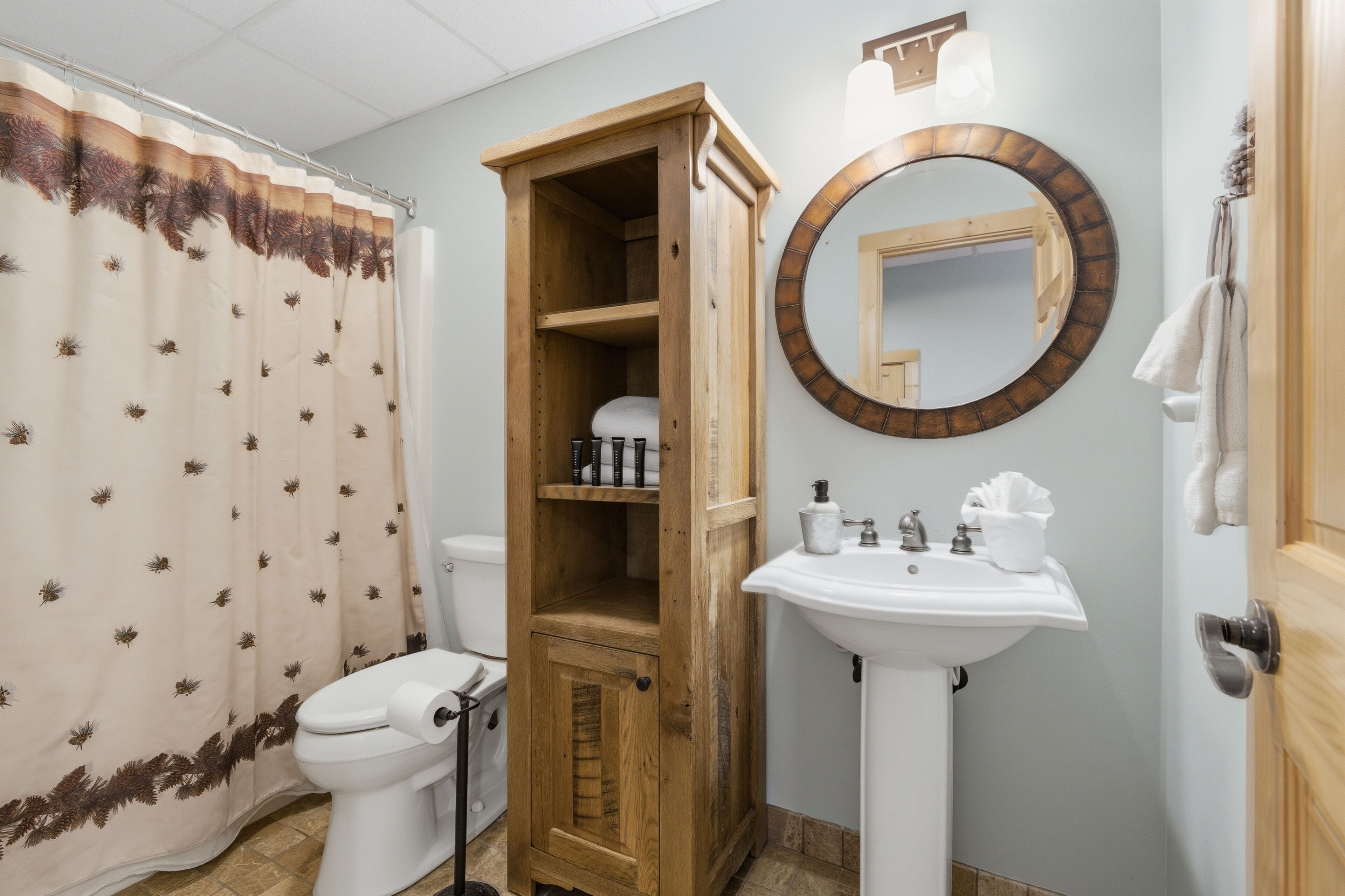 Un baño con inodoro, un armario de madera, un lavabo con espejo y una cortina de ducha.