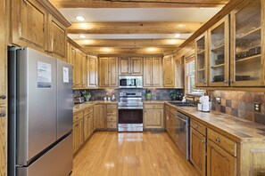 A kitchen with wooden cabinets, stainless steel appliances, and a tiled backsplash. - Pine Cone Cabin 4 Bedroom Cabin (Sevierville)