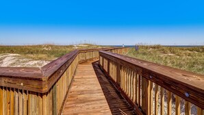 Ein hölzerner Steg führt zu einem Strand unter blauem Himmel.