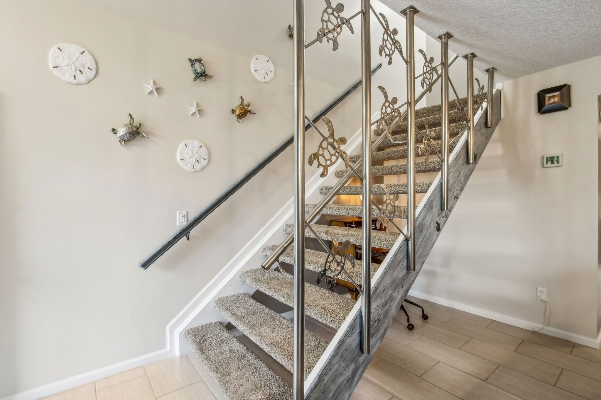 Eine Treppe mit Metallgeländer, Teppichstufen und Wanddekoration mit Motiven von Sternen und Schildkröten.