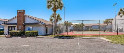 A building with a brick chimney, a parking lot, and a fenced tennis court.