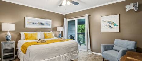 A bedroom with a bed, two bedside lamps, a ceiling fan, a chair, and a balcony with a view.