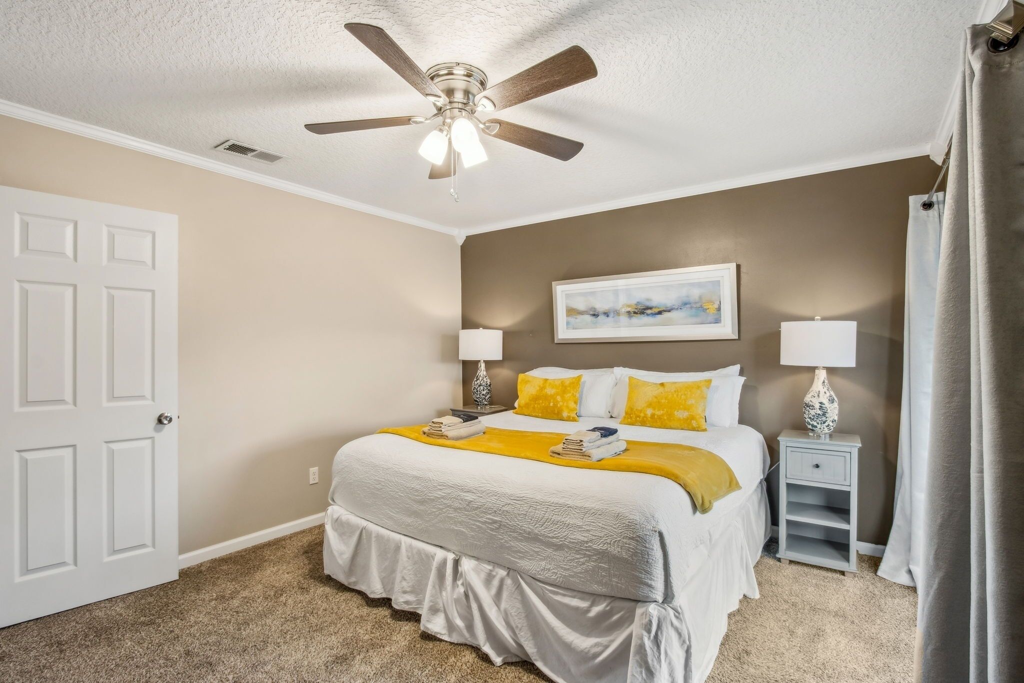 A bedroom with a bed, ceiling fan, bedside lamps, and a nightstand.