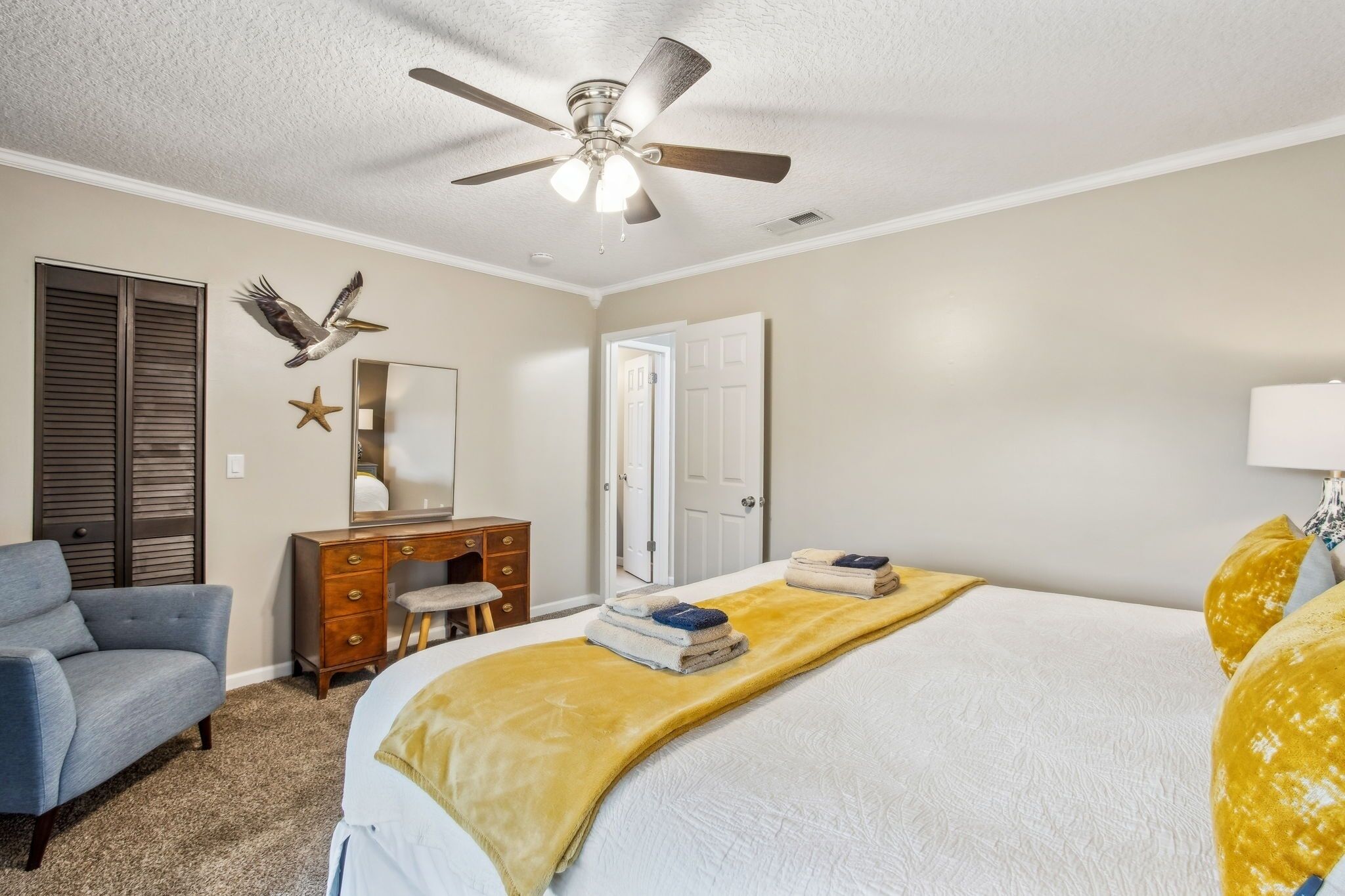 A bedroom with a bed, a desk, a chair, a ceiling fan, and a door.