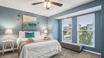 A bedroom with a bed, two bedside tables with lamps, a ceiling fan, a window with blinds, and a bench.