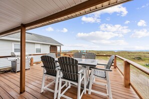 Une terrasse extérieure couverte, équipée d’une table et de chaises, d’un barbecue et offrant une vue sur la plage.