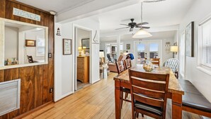 A spacious dining area with a wooden table and chairs, a ceiling fan, and a view of the kitchen in the background. - Spacious Beachfront Duplex - Top Floor - Dog Friendly 124 S Fletcher (Fernandina Beach)
