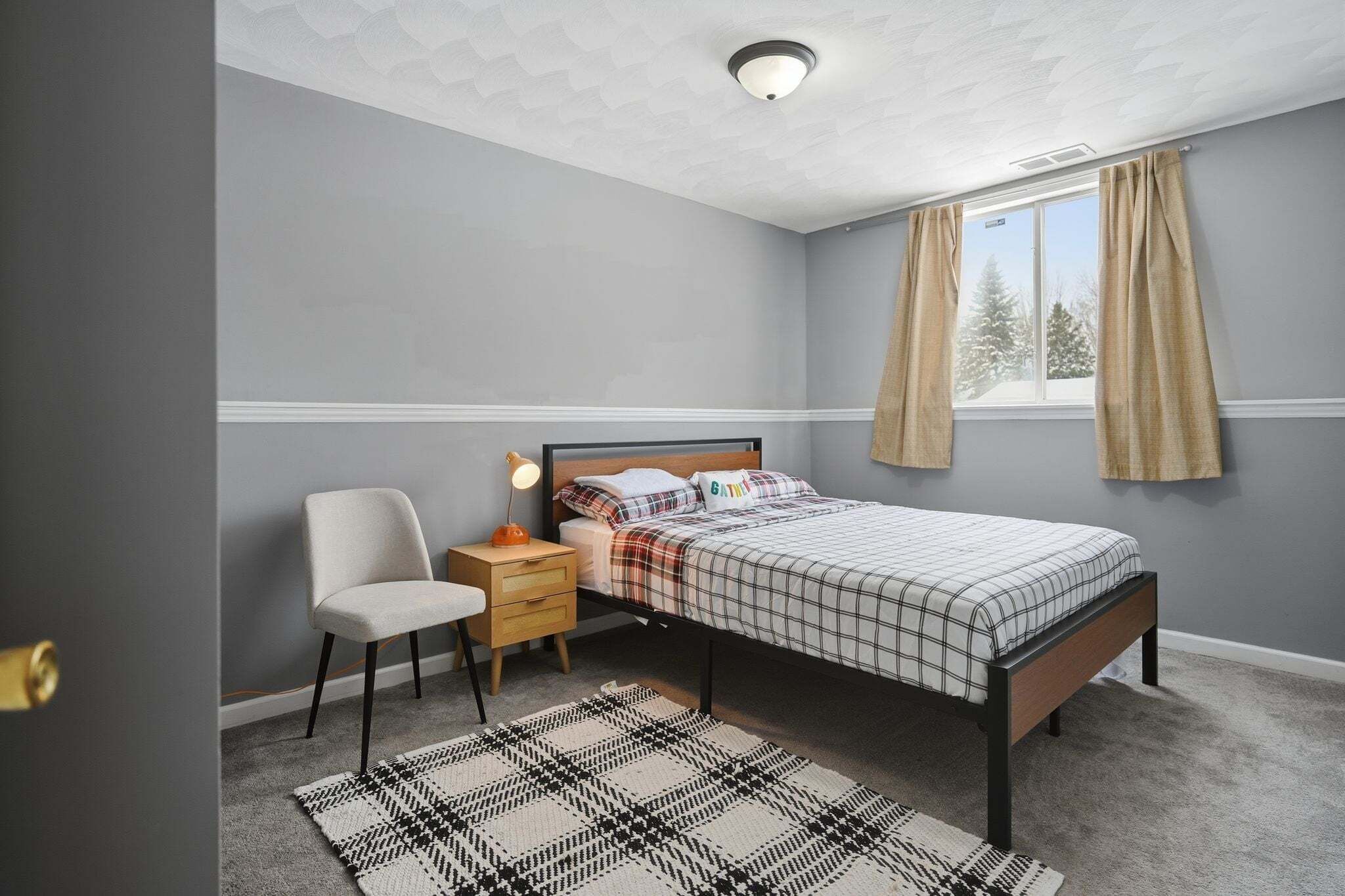 A bedroom with a bed, nightstand, chair, and window with curtains.