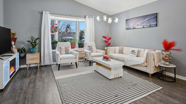 Ein modernes Wohnzimmer mit einer Couch, einem Couchtisch und einer TV-Konsole. An den Wänden befinden sich Pflanzen und ein Gemälde.