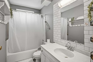 A modern bathroom with a bathtub, toilet, sink, and a large mirror. - Pet Friendly Lansing Home - Private Gym - Near MSU (Lansing)