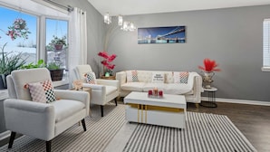 Ein modernes Wohnzimmer mit Sofa, Sessel und Couchtisch. Üppige Pflanzen und ein Gemälde zieren die Wand.
