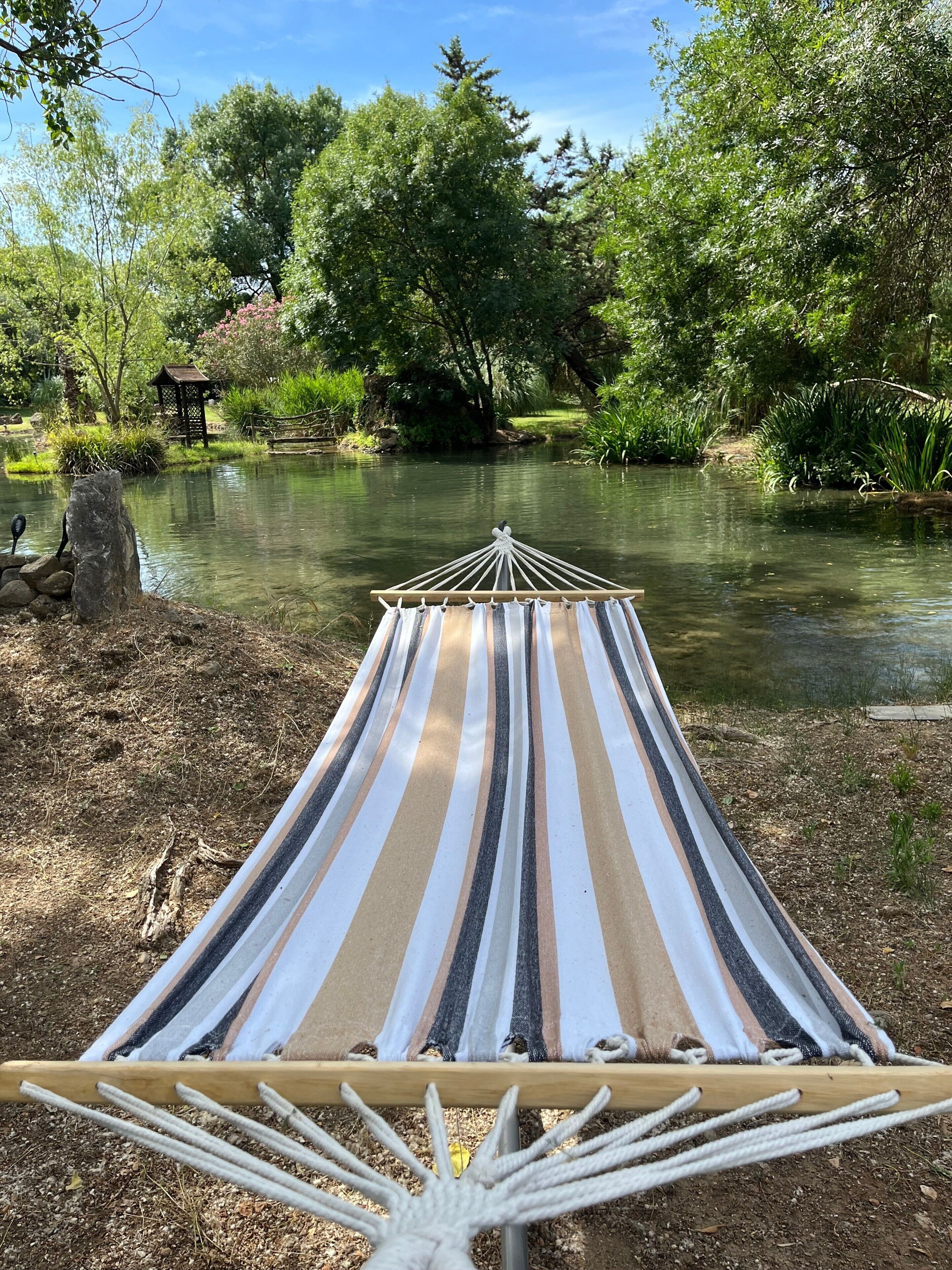 Una hamaca junto a un río tranquilo, rodeada de exuberante vegetación y una estructura de madera.