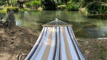 Una hamaca junto a un río tranquilo, rodeada de exuberante vegetación y una estructura de madera.