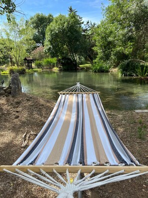 Un hamac au bord dâune riviĂšre paisible, entourĂ© dâune vĂ©gĂ©tation luxuriante et dâune structure en bois.