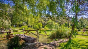 A serene garden with a wooden bridge, a pond, and lush greenery. - Domaine Saint Amour – Studio Océane: Romantic Getaway with Lake View, Pool & 2-Hectare Park (Trans-en-Provence)