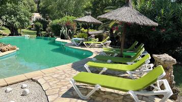 A pool area with lounge chairs, a stone-tiled deck, and a thatched umbrella.