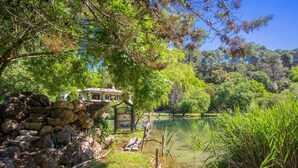 A rustic stone wall, a wooden bridge, and a house with a tiled roof by a calm lake. - Domaine Saint Amour – Gîte Au Lac: 2-Hectare Estate with Lake, Waterfall & Pool (Trans-en-Provence)