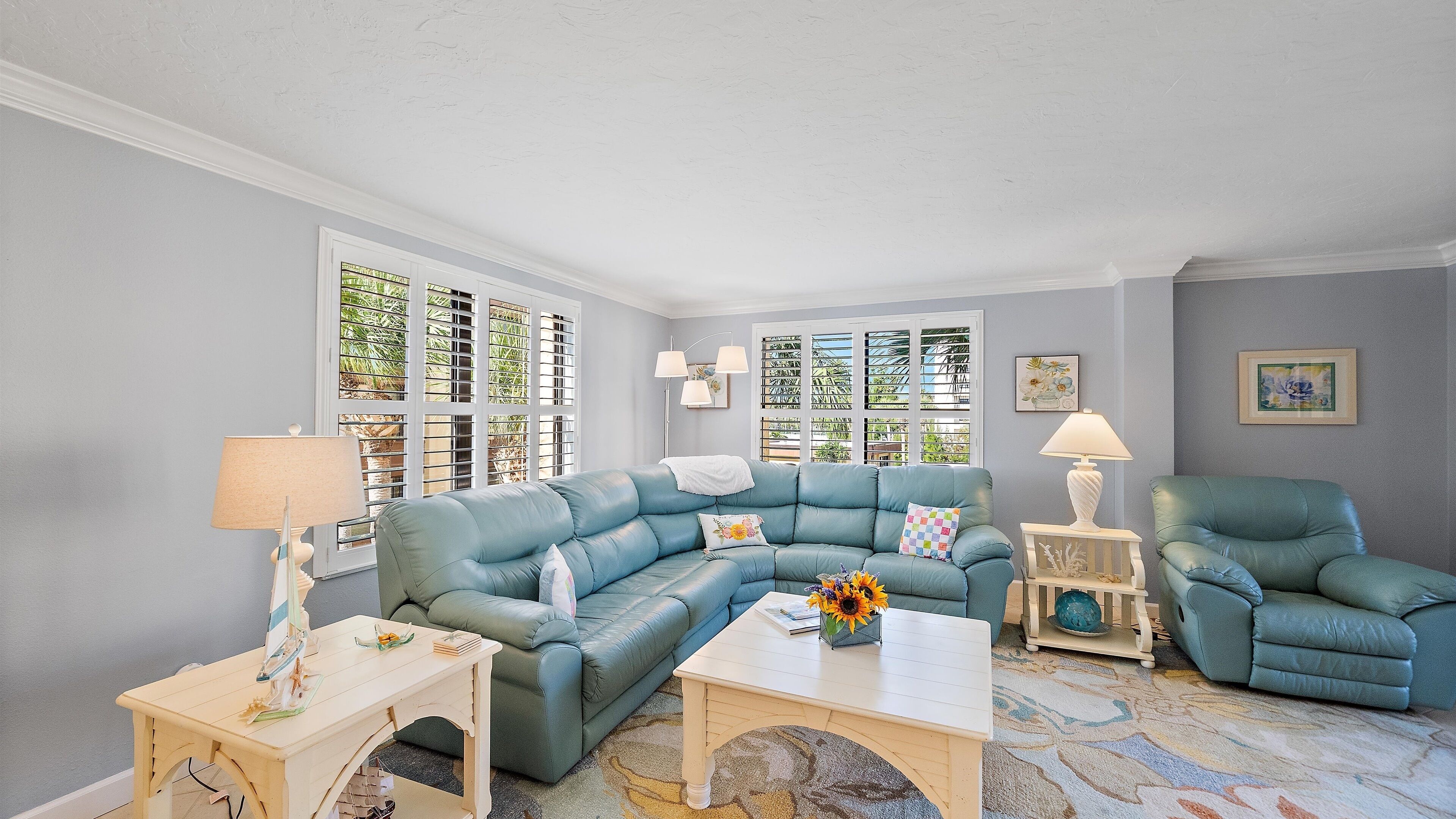 A living room with a blue sectional sofa, a small table with a lamp, and a window with blinds.