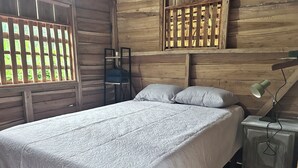 A wooden cabin room with a bed, a nightstand, and a window with a wooden lattice. - Eden travel Cabecars (Valle La Estrella)