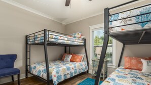 A bedroom with two bunk beds, a blue chair, and a window with blinds. - Bienville Bungalow - 304 Bienville Blvd 2 Bedroom Home (Dauphin Island)