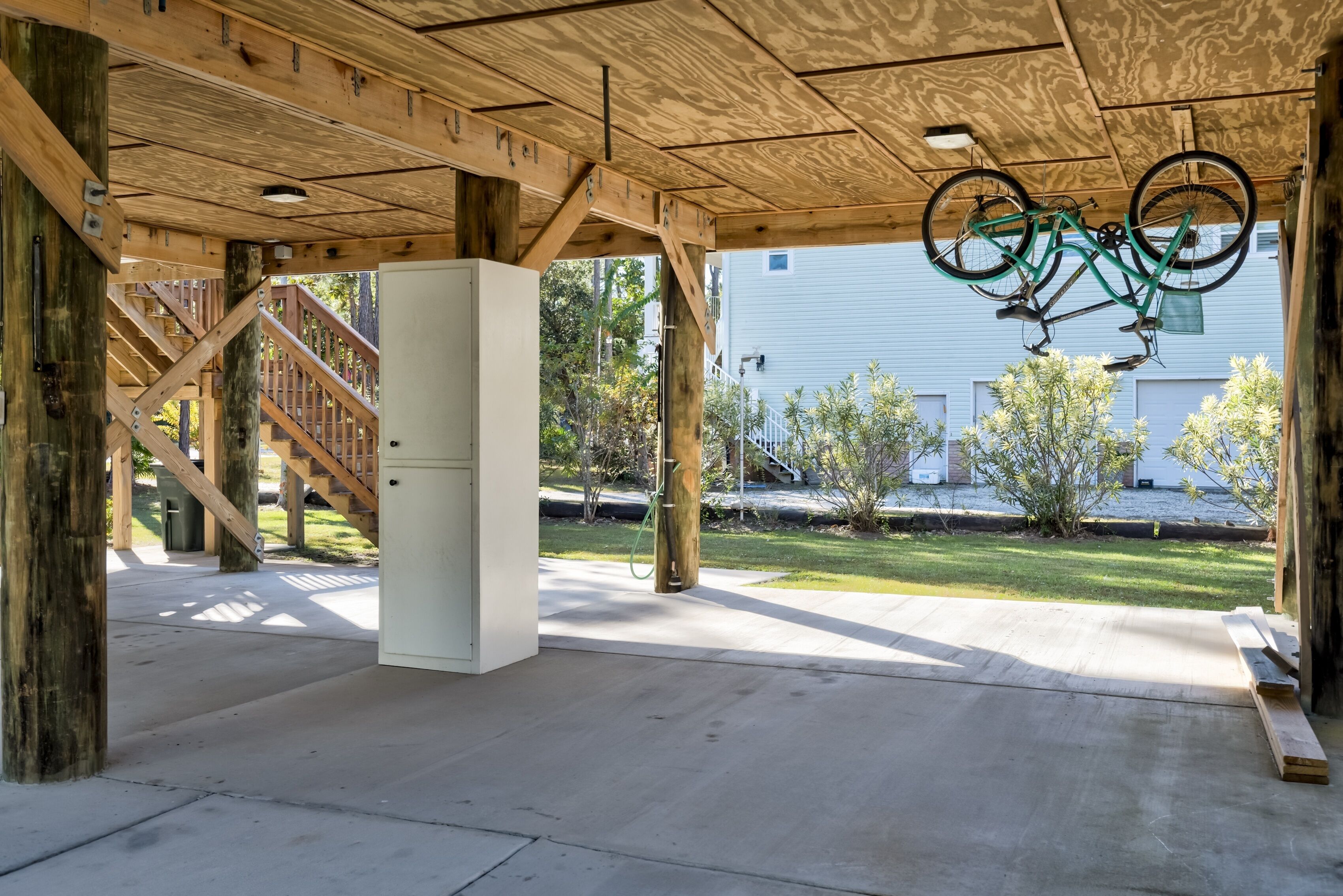 A covered outdoor area with a concrete floor, wooden beams, a white cabinet, and a bicycle hanging from the ceiling.
