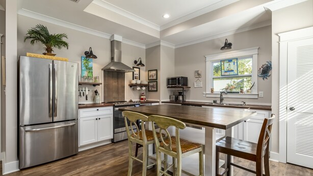 A modern kitchen with a stainless steel refrigerator, wooden chairs, and a large island. - Bienville Bungalow - 304 Bienville Blvd 2 Bedroom Home (Dauphin Island)