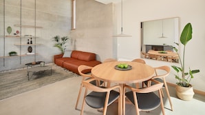 A modern living room with a round wooden dining table, leather sofa, and a large mirror on the wall.