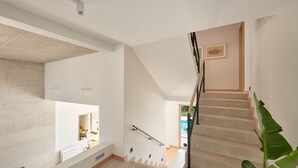 A modern staircase with a wooden handrail, a white wall with a picture, and a plant on the right.