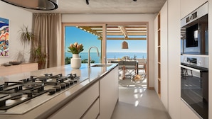 A modern kitchen with a central island, a built-in oven, and a view of the sea.