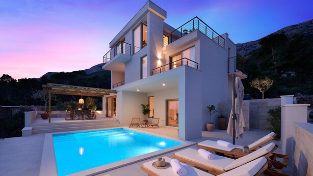A modern two-story house with a swimming pool, lounge chairs, and a patio area.