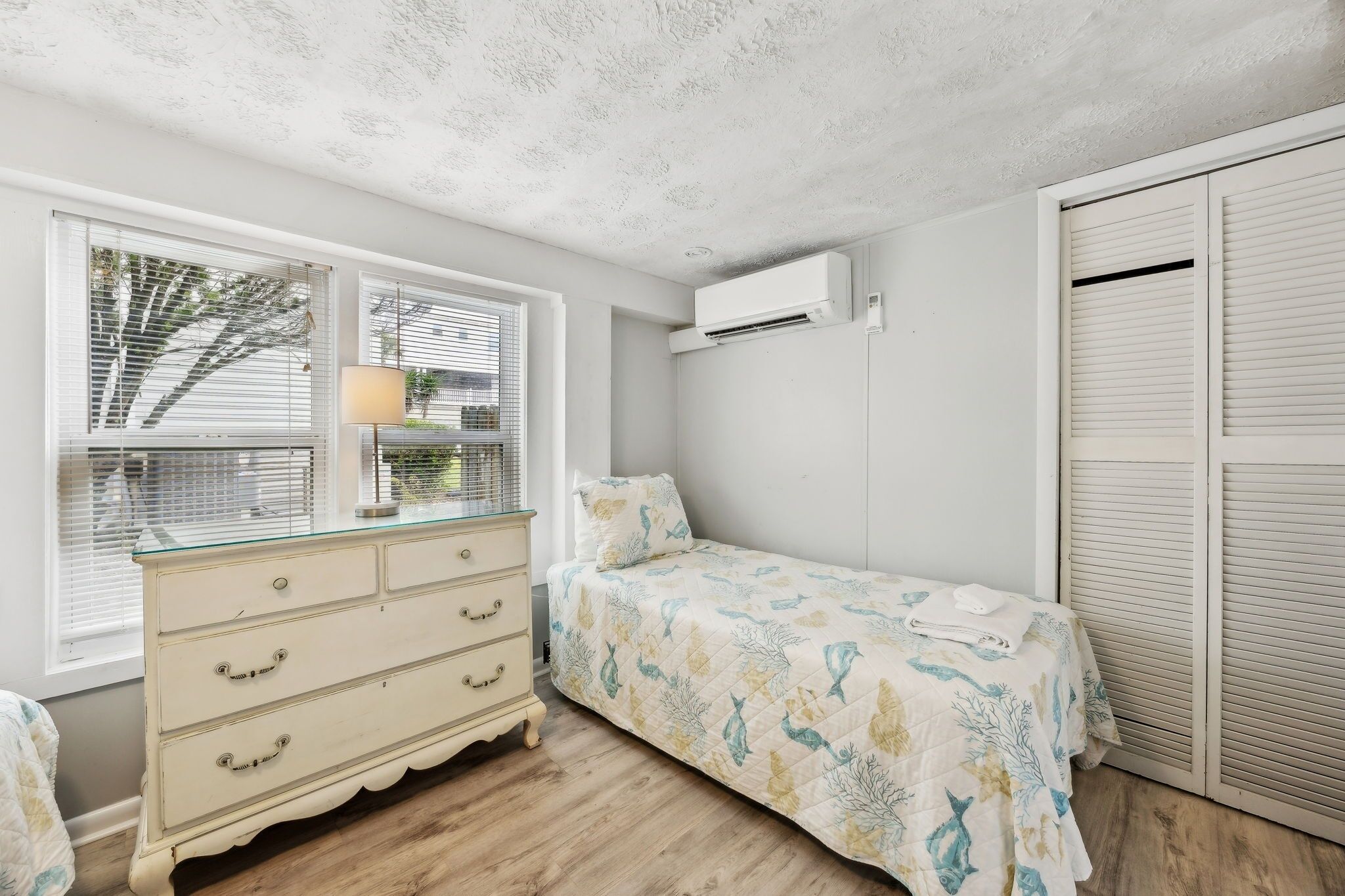A bedroom with a bed, dresser, window, and air conditioning unit.