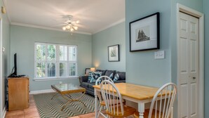 A dining area with a wooden table and white chairs, a ceiling fan, and a window with blinds. - Dauphin Luv B - Beach Club #201-b 2 Bedroom Condo (Dauphin Island)