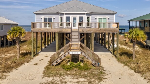 A beachfront house with a wooden deck and a staircase leading to a covered area. - Bay Breeze - 2420 Bienville 4 Bedroom Home (Dauphin Island)