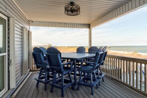 A covered outdoor deck with a table and chairs, overlooking a beach. - Bay Breeze - 2420 Bienville 4 Bedroom Home (Dauphin Island)
