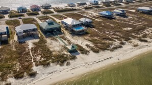 An aerial view of a coastal area with multiple beachfront properties, including houses and beach huts, connected by pathways and featuring direct ocean views. - Bay Breeze - 2420 Bienville 4 Bedroom Home (Dauphin Island)