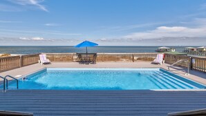 A swimming pool with lounge chairs and a blue umbrella on a deck with a view of the ocean. - Bay Breeze - 2420 Bienville 4 Bedroom Home (Dauphin Island)