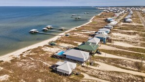 An aerial view of a coastal area with beach houses, a pier, and boats. - Bay Breeze - 2420 Bienville 4 Bedroom Home (Dauphin Island)