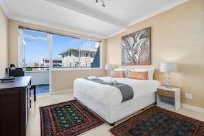 A bedroom with a large bed, a desk, a chair, and a window with a view of buildings. - Sailaway Sea Point (Cape Town)
