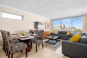 A modern living room with a dining area, large windows, and a city view. - Sailaway Sea Point (Cape Town)