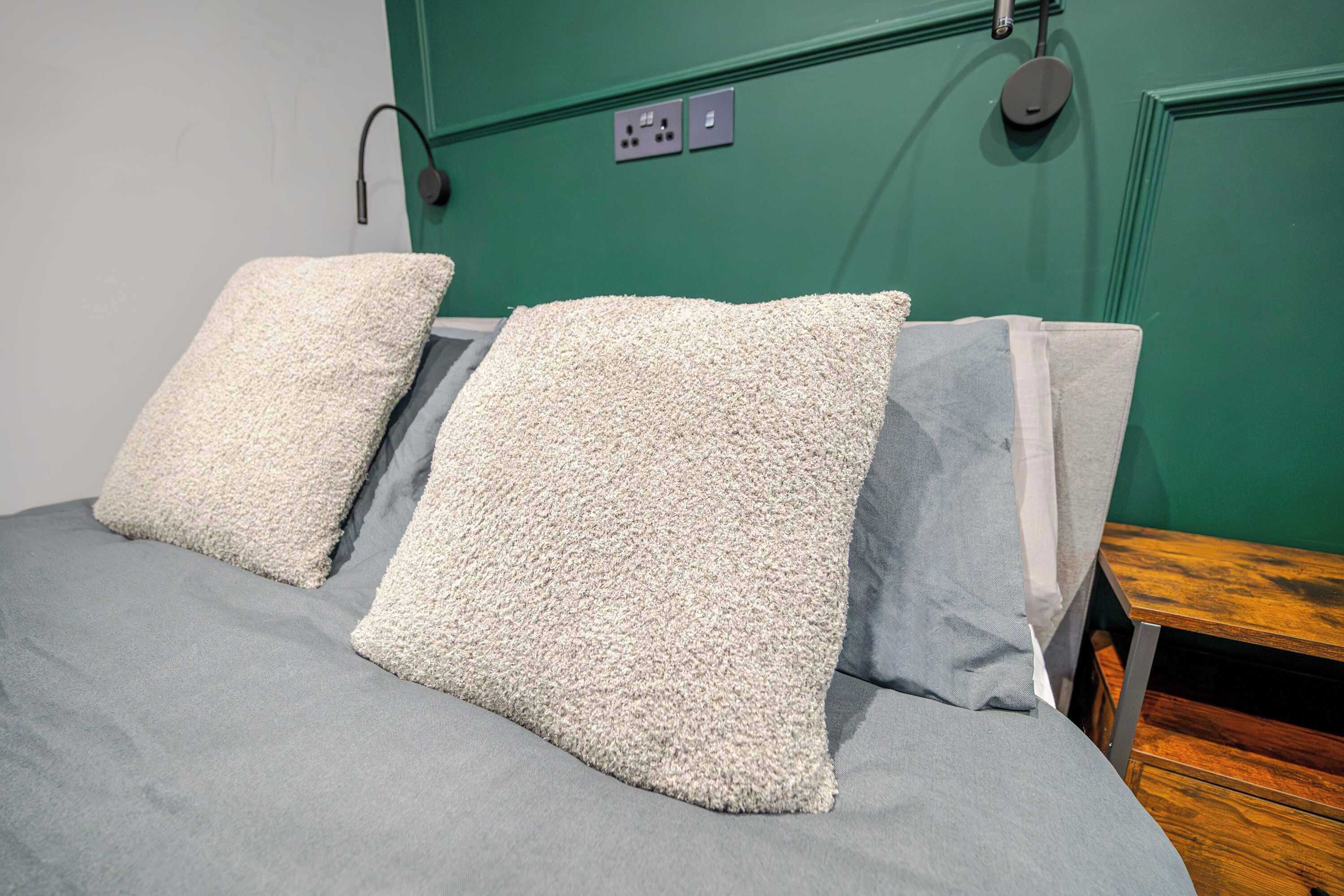 A bed with two pillows, a green wall, and a wooden nightstand.